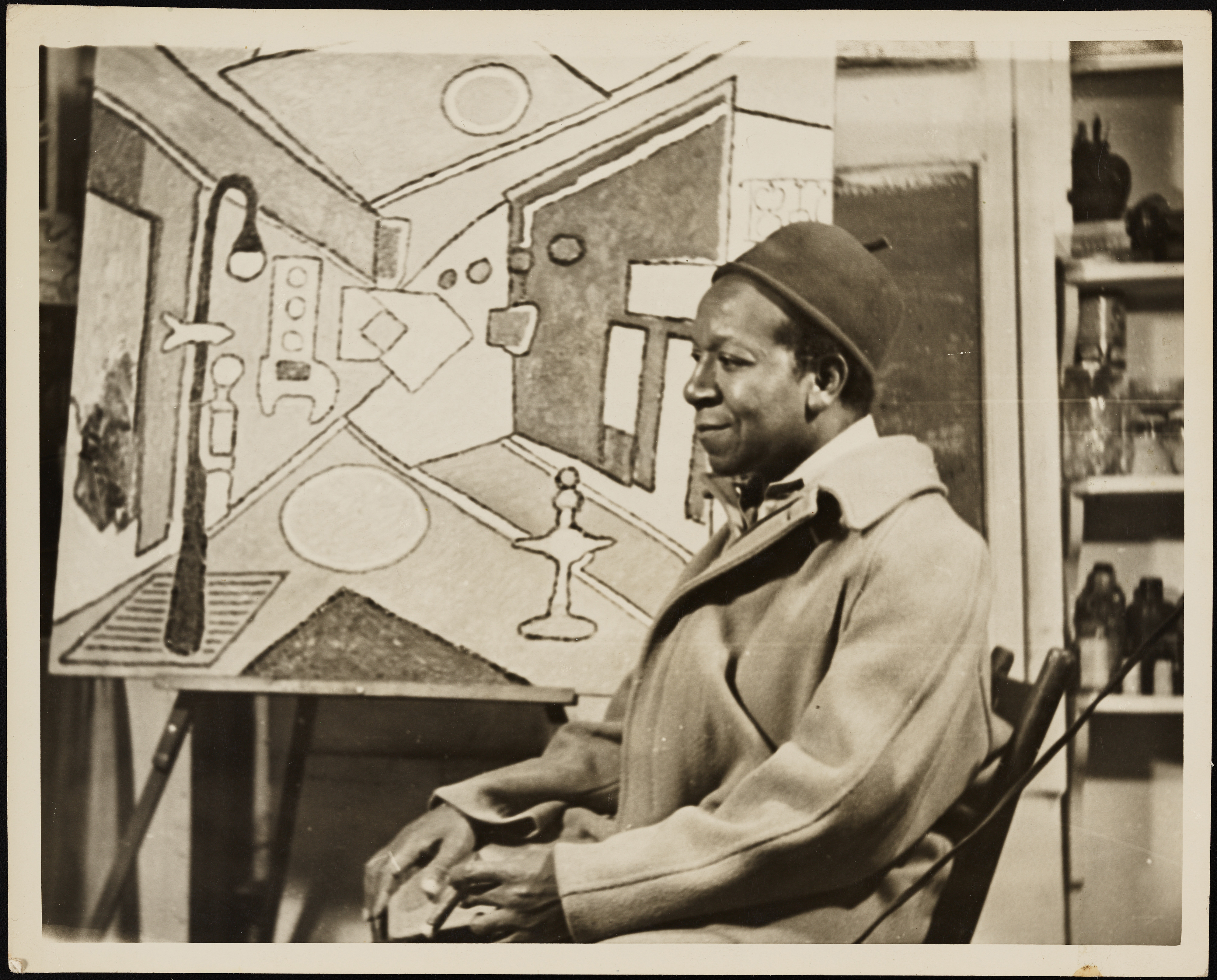 Delaney seated before one of his abstract paintings of a streetscape.